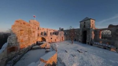 Kışın gün batımında tepedeki güzel tarihi şatonun havadan görünüşü harabeye döner. Tenczyn Kalesi, Polonya. FPV insansız hava aracı ile çekildi.