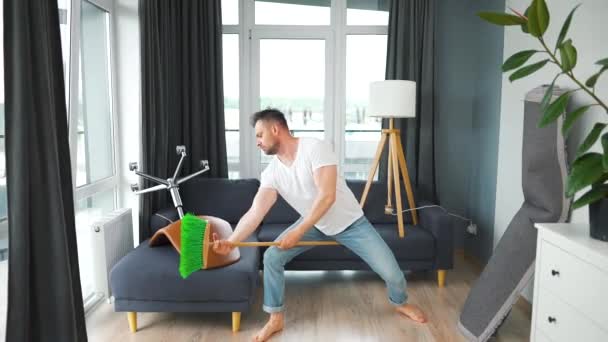 Hombre limpiando la casa y divirtiéndose bailando con una escoba. Movimiento lento — Vídeos de Stock