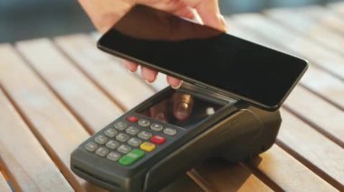 Akıllı telefondan yapılan temassız ödeme. Kablosuz ödeme konsepti. Yakın plan, kadın banka terminalindeki siparişi ödemek için akıllı telefon nakitsiz cüzdan teknolojisi kullanıyor..