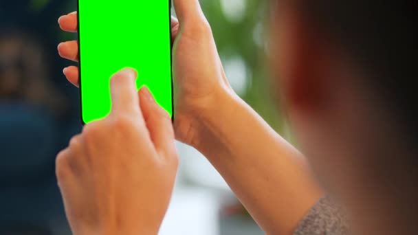 垂直モードで緑のモックアップ画面とスマートフォンを使用して自宅で女性。女の子はインターネットを閲覧し、コンテンツ、ビデオを見る — ストック動画