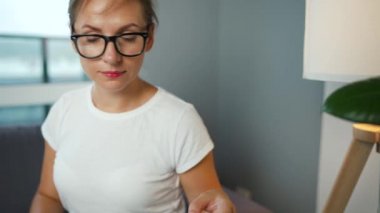 Gözlüklü bir kadın rahat bir odada kanepeye oturur ve kredi kartı ve dizüstü bilgisayar kullanarak online alışveriş yapar. İnternetten alışveriş, yaşam tarzı teknolojisi.