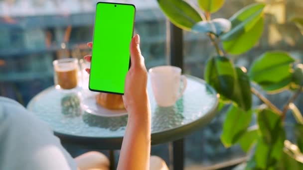 Женщина сидит в кафе и использует смартфон с зеленым макетом экрана в вертикальном режиме. Девочки просматривают Интернет, смотрят контент, видео, блоги. — стоковое видео