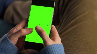 Adam dikey modda yeşil ekran ile akıllı telefon kullanıyor. İnternette gezinen, içeriği izleyen, videolar.