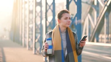 Paltolu beyaz bir iş kadınının portresi, soğuk bir sabahta şehirde dolaşıyor, kahve içiyor ve akıllı telefon kullanıyor. İletişim, iş günü, yoğun yaşam konsepti. Yavaş çekim