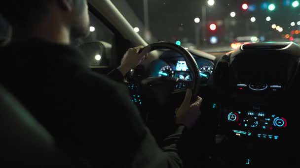 Un hombre conduciendo por las calles de la ciudad nocturna. Vista desde el asiento trasero del coche. — Vídeos de Stock