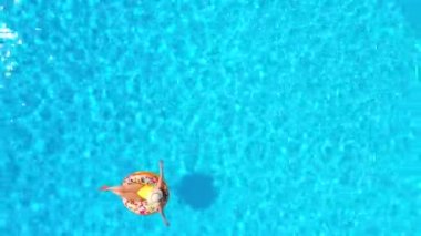 Havuzda donutun üzerinde yatan sarı mayo giymiş bir kadının hava manzarası.