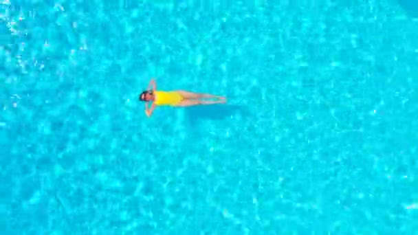 En tepeden, havuzda sırtüstü uzanmış sarı mayo giymiş bir kadın görüntüsü. Rahatlatıcı kavram — Stok video