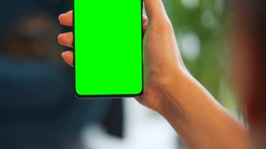 Evde dikey modda yeşil ekranlı akıllı telefon kullanan bir kadın var. Kız internette geziniyor, içeriği izliyor, videolar