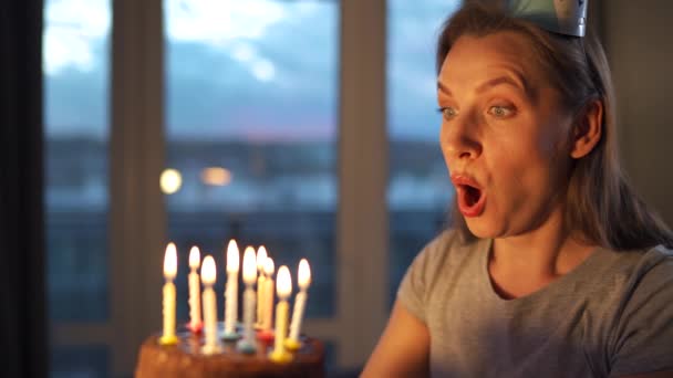 Lykkelig, spent kvinne som ønsker seg noe og blåser lys på en kake, feirer bursdag hjemme, sakte film – stockvideo