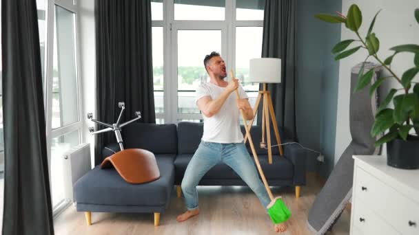 Człowiek sprzątający dom i bawiący się śpiewa miotłą. Zwolniony ruch — Wideo stockowe