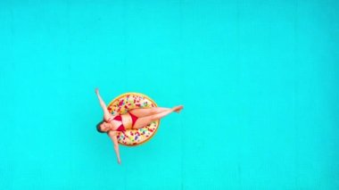 Havuzda donutun üzerinde yüzen kırmızı bikinili bir kadının hava görüntüsü.