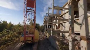 FPV insansız hava aracı, terk edilmiş sanayi binaları ve bir kazıcının etrafında hızla ve manevra kabiliyetiyle uçar..