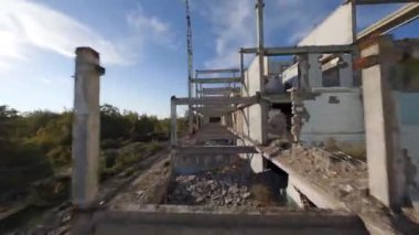 FPV insansız hava aracı, terk edilmiş sanayi binaları ve bir kazıcının etrafında hızla ve manevra kabiliyetiyle uçar..