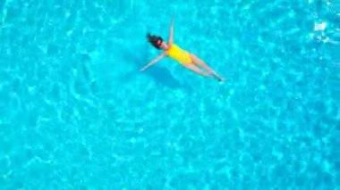 En tepeden, havuzda sırtüstü uzanmış sarı mayo giymiş bir kadın görüntüsü. Rahatlatıcı kavram