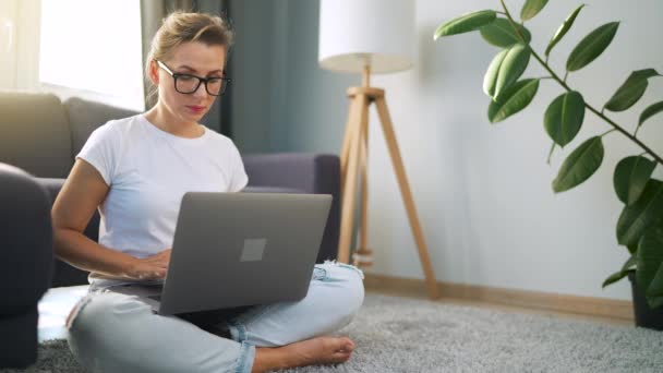 Mulher com óculos está sentada no chão e trabalhando em um laptop. Conceito de trabalho remoto. — Vídeo de Stock