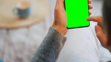 Evde dikey modda yeşil ekranlı akıllı telefon kullanan bir kadın var. Kız internette geziniyor, içeriği izliyor, videolar