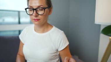 Gözlüklü bir kadın rahat bir odada kanepeye oturur ve kredi kartı ve dizüstü bilgisayar kullanarak online alışveriş yapar. İnternetten alışveriş, yaşam tarzı teknolojisi.