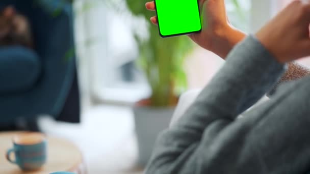 Γυναίκα στο σπίτι χρησιμοποιώντας smartphone με πράσινη οθόνη mock-up σε κάθετη λειτουργία. Κορίτσι περιήγηση στο Internet, παρακολουθώντας περιεχόμενο, βίντεο — Αρχείο Βίντεο