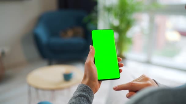 Mulher em casa usando smartphone com tela verde mock-up no modo vertical. Menina navegando na Internet, assistindo conteúdo, vídeos. VPO — Vídeo de Stock