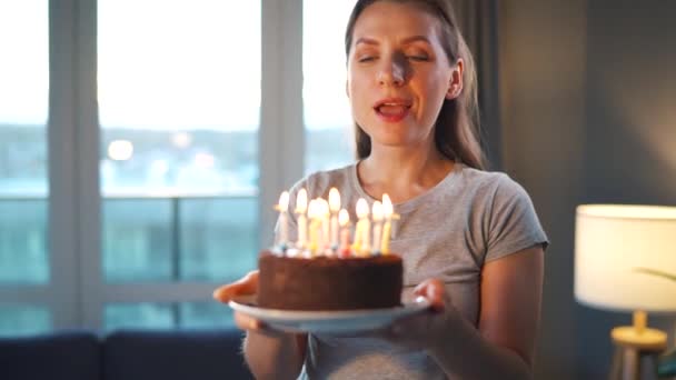Onnellinen innoissaan nainen tekee vaalia toive ja puhaltaa kynttilöitä loma kakku, juhlii syntymäpäivää kotona — kuvapankkivideo