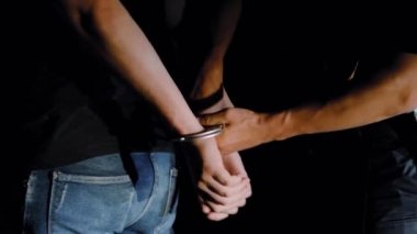 Polis memuru gece tutuklanan adama kelepçe takıyor ve onu polis arabasına götürüyor.