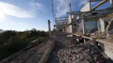 FPV insansız hava aracı, terk edilmiş sanayi binaları ve bir kazıcının etrafında hızla ve manevra kabiliyetiyle uçar..
