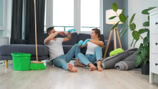 Pasangan lelah duduk di lantai di sebuah ruangan dan saling tos setelah mereka selesai membersihkan rumah. Gerakan lambat — Stok Video