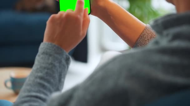 Vrouw thuis met smartphone met groene mock-up scherm in verticale modus. Meisje surfen op internet, kijken naar inhoud, video 's — Stockvideo