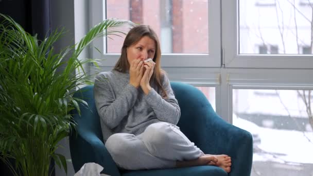 Una mujer malsana se sienta en una silla y tose porque tiene un resfriado, gripe, coronavirus. Está nevando afuera. — Vídeos de Stock