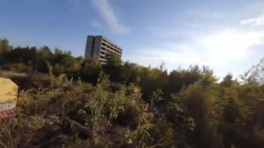 FPV insansız hava aracı, terk edilmiş sanayi binaları ve bir kazıcının etrafında hızla ve manevra kabiliyetiyle uçar..