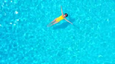 En tepeden, havuzda sırtüstü uzanmış sarı mayo giymiş bir kadın görüntüsü. Rahatlatıcı kavram