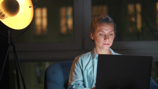Kobieta siedzi w fotelu i pracuje w nocy nad laptopem. Pojęcie pracy zdalnej. — Wideo stockowe