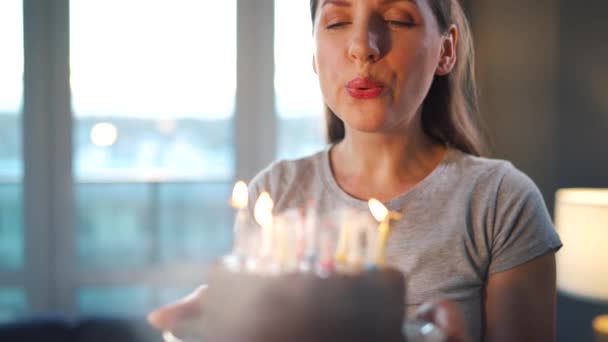 Onnellinen innoissaan nainen tekee vaalia toive ja puhaltaa kynttilöitä loma kakku, juhlii syntymäpäivää kotona, hidastettuna — kuvapankkivideo
