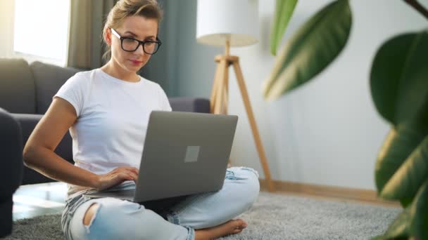Mujer con gafas está sentado en el suelo y trabajando en un ordenador portátil. Concepto de trabajo remoto. — Vídeo de stock