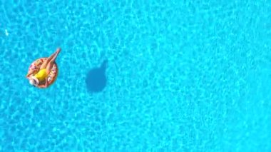 Havuzda donutun üzerinde yatan sarı mayo giymiş bir kadının hava manzarası.