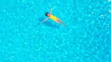 En tepeden, havuzda sırtüstü uzanmış sarı mayo giymiş bir kadın görüntüsü. Rahatlatıcı kavram