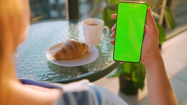 Mujer sentada en un café y usando smartphone con pantalla verde en modo vertical. Chica navegando por Internet, viendo contenido, videos, blogs. — Vídeos de Stock