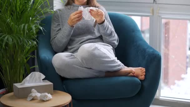 Ohälsosam kvinna sitter i en stol och hostar eftersom hon har förkylning, influensa, coronavirus. Det snöar ute — Stockvideo