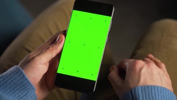 Man använder smartphone med grön mock-up skärm i vertikalt läge. Man surfar på Internet, tittar på innehåll, videor. — Stockvideo