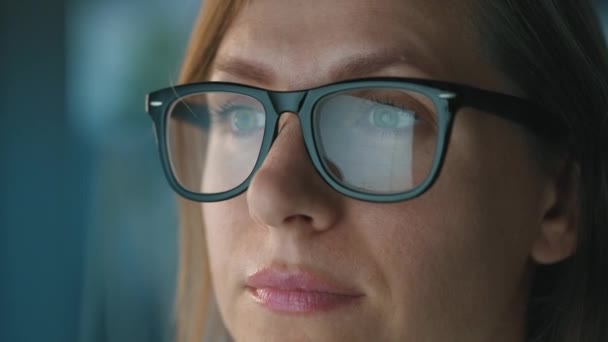 Mulher de óculos a olhar para o monitor e a trabalhar com gráficos e análises. A tela do monitor é refletida nos óculos. Trabalho à noite. Extremo close-up — Vídeo de Stock