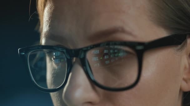 Γυναίκα με γυαλιά που κοιτάζει στην οθόνη και εργάζεται με δεδομένα και αναλυτικά στοιχεία. Η οθόνη της οθόνης αντανακλάται στα γυαλιά. Δουλειά τη νύχτα. Πολύ κοντινό πλάνο. — Αρχείο Βίντεο