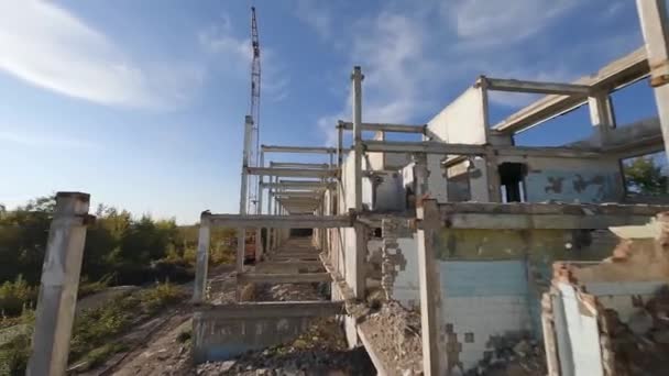 El dron FPV vuela suavemente entre edificios industriales abandonados y alrededor de una excavadora. — Vídeos de Stock