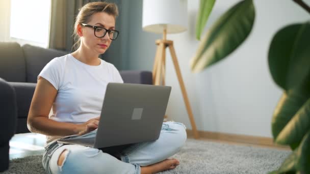 Женщина в очках сидит на полу и работает над ноутбуком. Кэт на заднем плане. Концепция дистанционной работы. — стоковое видео