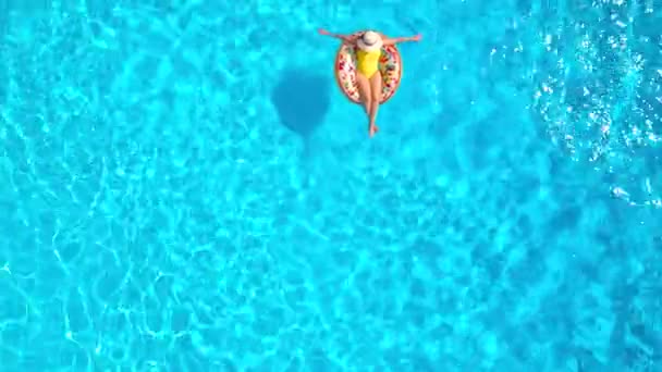 Вид с воздуха на женщину в жёлтом купальнике, лежащую на пончике в бассейне — стоковое видео