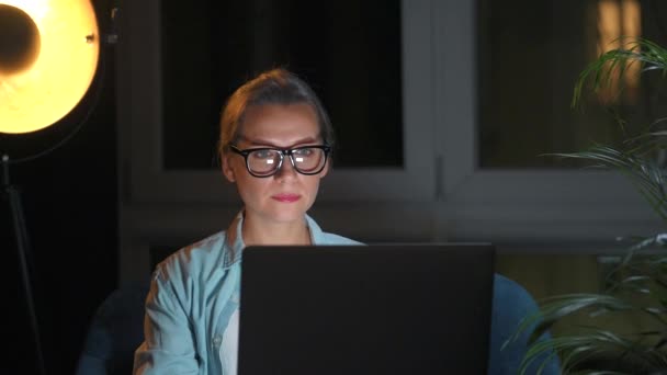 Femme est assise dans le fauteuil et travaille sur un ordinateur portable la nuit ou envoyer un texto à quelqu'un. Concept de télétravail. — Video