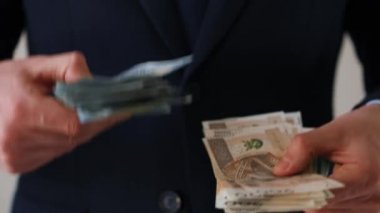 Resmi olarak giyinmiş bir adam Amerikan doları ve Polonya zloti banknotlarını tutuyor ve karşılaştırıyor. Yatırım, başarı, finansal beklentiler veya kariyer ilerlemesi kavramı