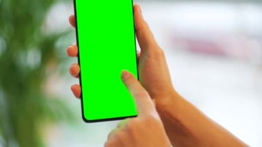 Evde dikey modda yeşil ekranlı akıllı telefon kullanan bir kadın var. Kız internette geziniyor, içeriği izliyor, videolar izliyor. POV.