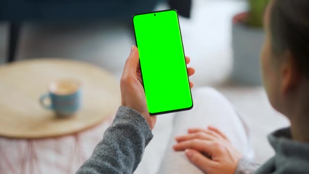 Mujer en casa usando smartphone con pantalla verde en modo vertical. Chica navegando por Internet, viendo contenido, videos — Vídeo de stock