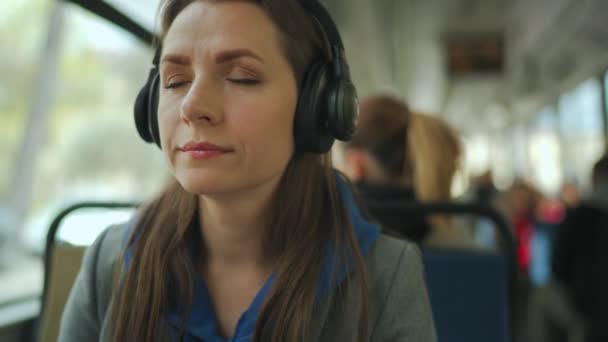 Женщина слушает подкаст или музыку во время путешествий в общественном транспорте. Город, город, транспорт. — стоковое видео