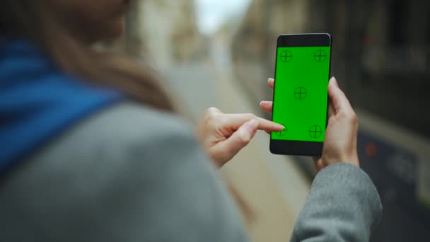 Kvinna på gatan med hjälp av smartphone med grön prototyp skärm i vertikalt läge mot bakgrund av en passerande spårvagn. — Stockvideo